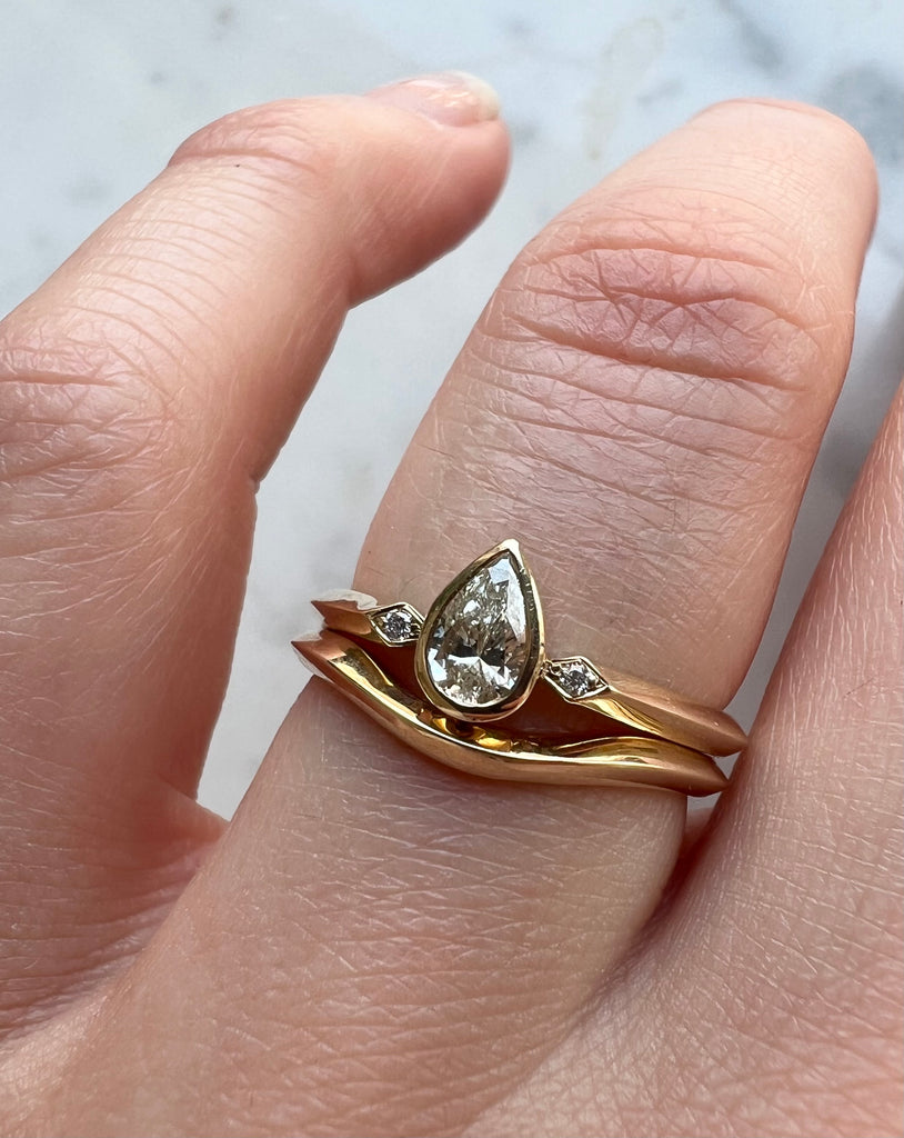 Pear shaped diamond ring being worn with a curved shaped wedding ring 