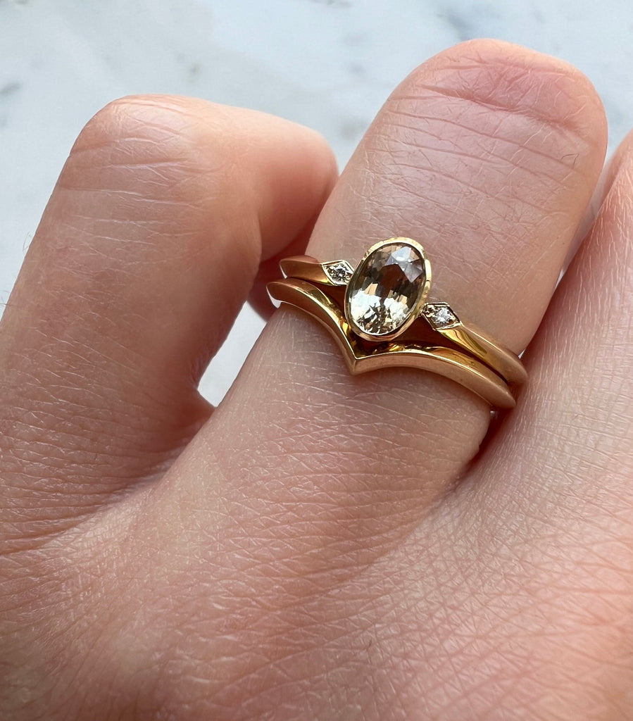 Peach coloured sapphire and diamond ring being worn with wishbone wedding band